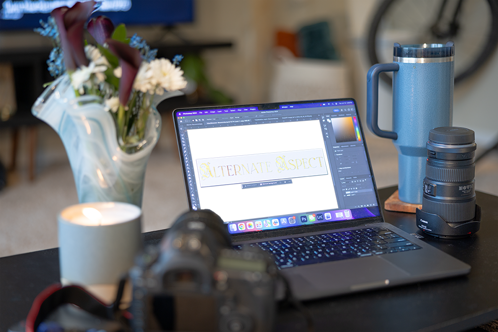 Laptop displaying a custom logo design in Photoshop beside professional camera equipment in a Breckenridge branding studio